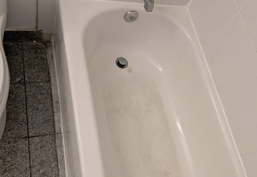 Bathtub with soap scum and a grimy floor edge before deep cleaning